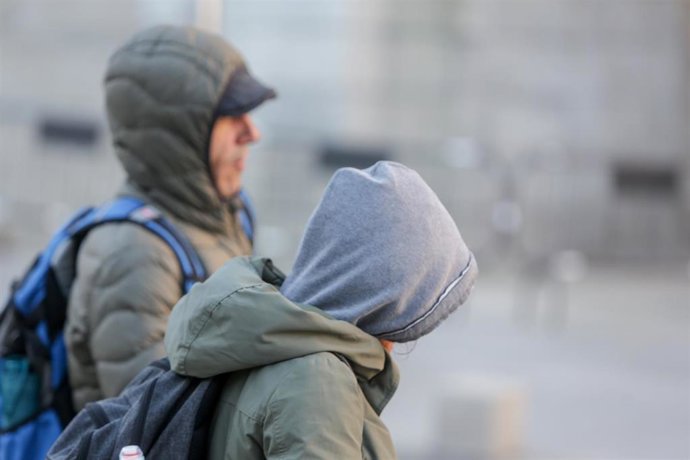 Dos jovenes se protegen del frío con abrigos y gorros mientras .