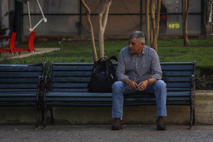 Un hombre sentado en un banco en una calle de Santiago