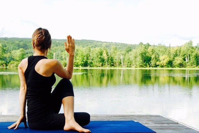 Mujer haciendo yoga junto a un lago.