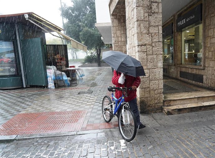 Un ciclista con un pagaguas resguardándose de la lluvia y el viento