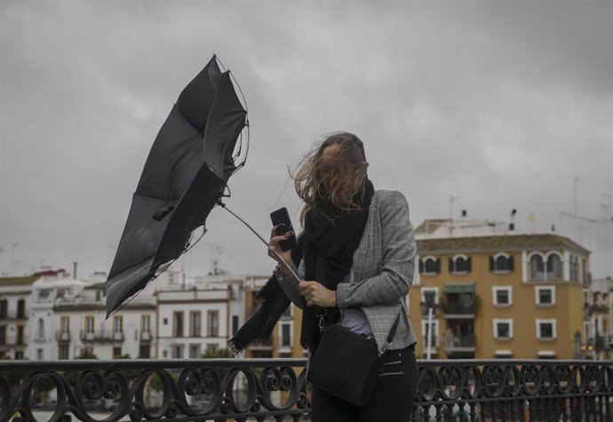 Una racha de viento desbarata el paragüas de una viandante mientras camina por el Puente de Isabel II. En Sevilla, (Andalucía), a 22 de noviembre de 2019.