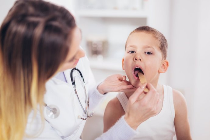 Female doctor examining child with tongue depressor at surgery