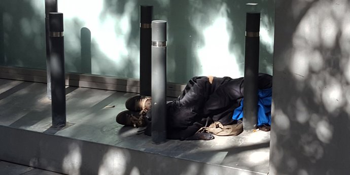 Una persona durmiendo en la calle entre bolardos. Imagen de recurso para sin techo, sin hogar, sinhogarismo