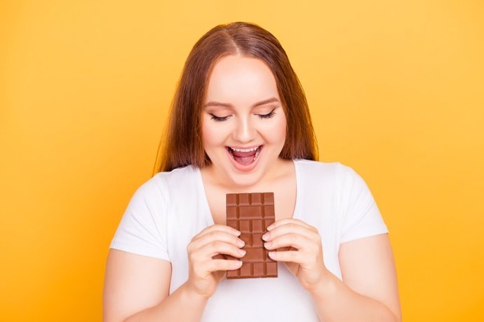 Concepto de cuidado corporal. Mujer mirando la barra de chocolate que va a morder. Dulce, adicción, compulsión por el chocolate.