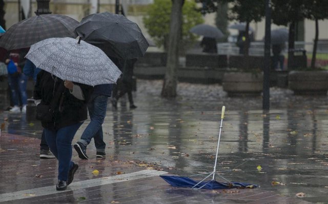 Personas se protegen de la lluvia bajo sus paragüas durante la borrasca 'Elsa'