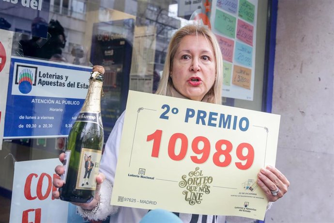 Adela, la dueña de la administración de lotería 'Los Buhítos de la 31' situada en la calle Felix Boix, 4 de Madrid, posa con el segundo premio, el número 10989, que se ha distribuído en su local, en Madrid (España), a 22 de diciembre de 2019.
