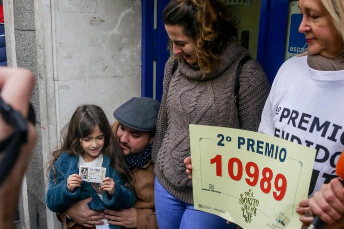 Carmen (d), la dueña de la administración de lotería 'Los Buhítos de la 31' situada en la calle Felix Boix, 4 de Madrid, junto a una familia de agraciados con el segundo premio, el número 10989, parte del cual,  se ha distribuído en su local, en Madrid 