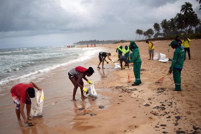 Empleados municipales y voluntarios trabajan para retirar manchas de petróleo en una playa de Camacari, municipio de Bahía, en el oeste del país.