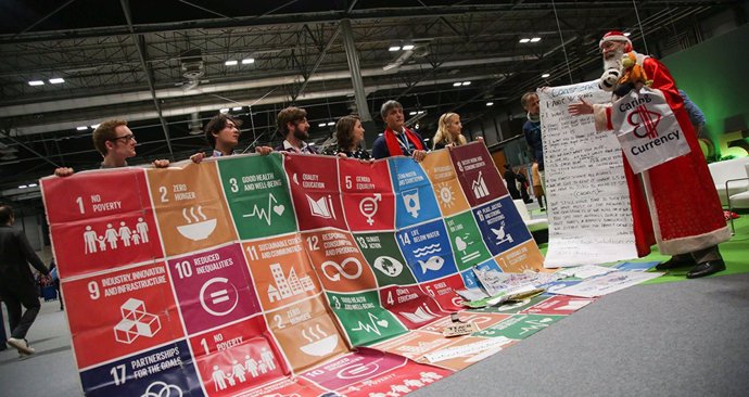 El personaje 'SustainaClaus' junto a un cartel de los Objetivos de Desarrollo Sostenible (ODS) de la Agenda 2030.