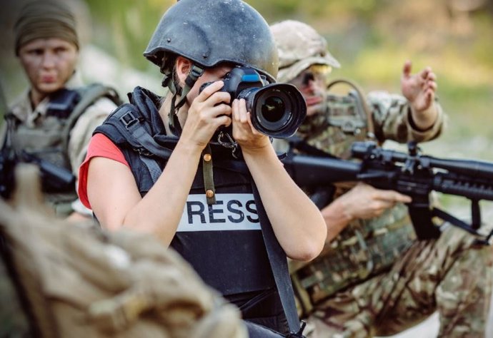 Periodista amb armilla i casc entre individus armats