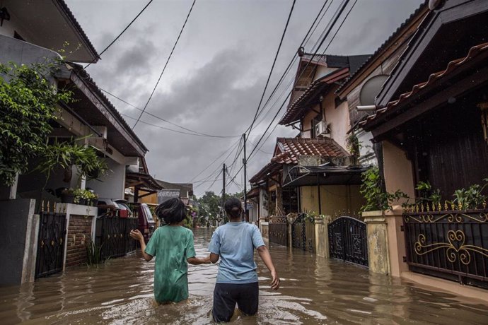 Dos mujeres andan a través de una calle inundada después de las intensas lluvias que han caído en la capital de Indonesia durante la víspera de Año Nuevo.
