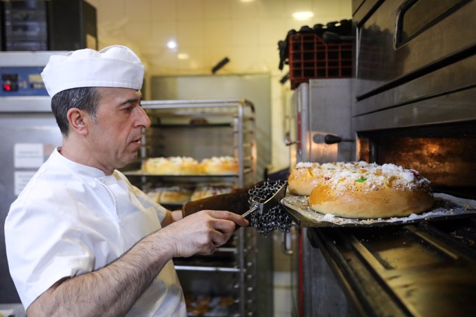Un pastelero saca del horno los roscones de Reyes recién hechos de forma artesanal en la Pastelería Horno de San Onofre-La Santiaguesa