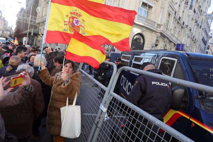 Una mujer porta dos banderas de España cerca de un furgón de policía en la calle Génova