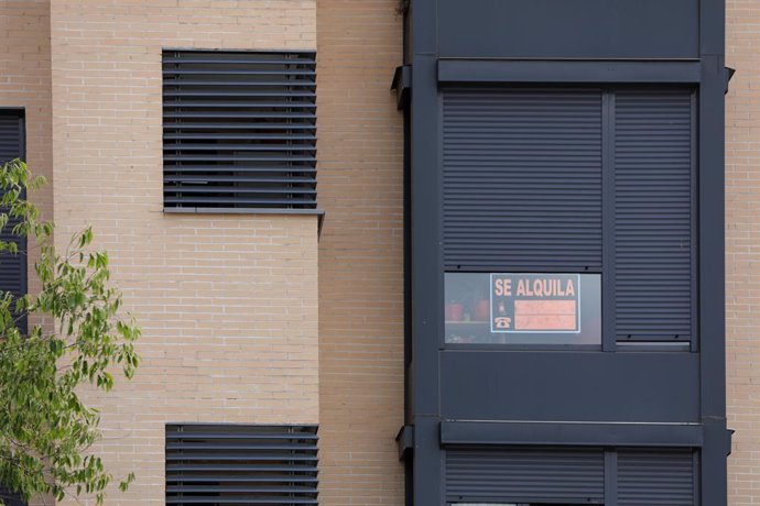 En la fachada de un edificio se ve un cartel de 'Se Alquila' bajo la persiana de uno de los pisos.