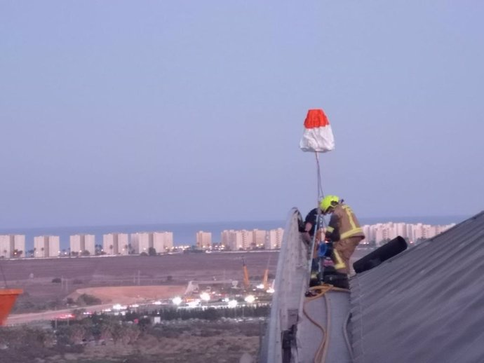 Dos bomberos trabajan sobre la cornisa del aeropuerto con la playa de Urbanova al fondo.