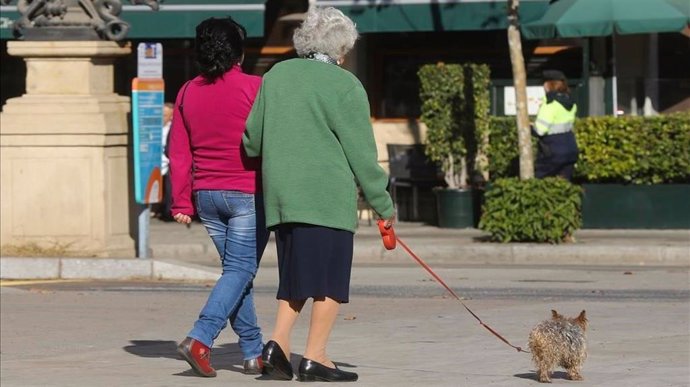 Una mujer pasea junto con una persona mayor y su perro