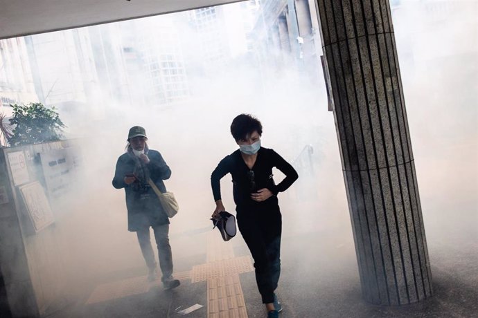 Personas corriendo en medio de gases lacrimógenos durante una protesta en Hong Kong