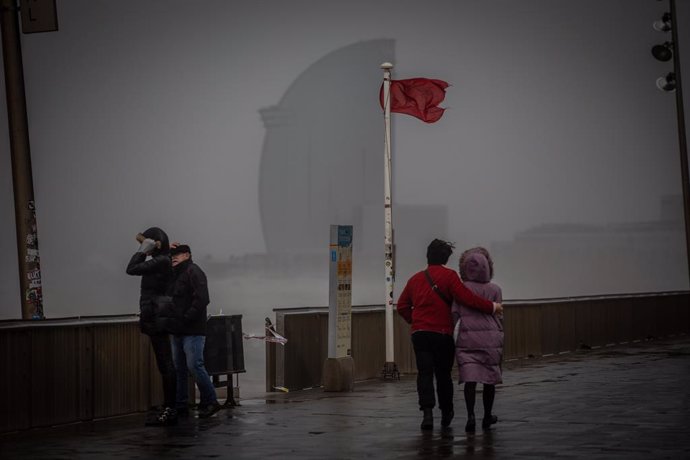 Diverses persones passegen al costat de la bandera vermella de la platja al passeig marítim de Barcelona, on la borrasca Gloria ha deixat fortes ratxes de vent i pluja, 21 de gener del 2020.