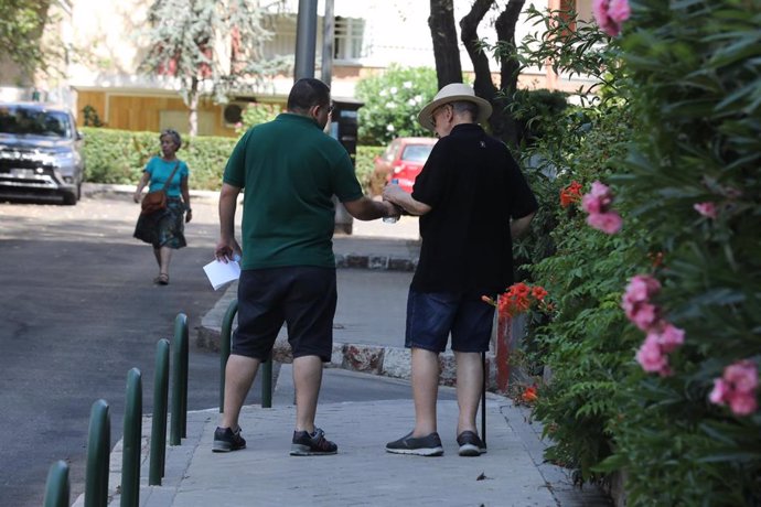 Un hombre le da una botella de agua a un anciano, mientras pasean por una calle de Madrid.