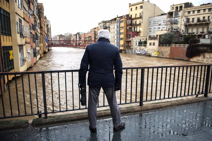 Un hombre pasea por uno de los puentes que sobrepasa el rio Onyar, a punto de desbordarse, debido a las fuertes lluvias que ha dejado la borrasca 'Gloria', en Girona /Catalunya (España), a 22 de enero de 2020.