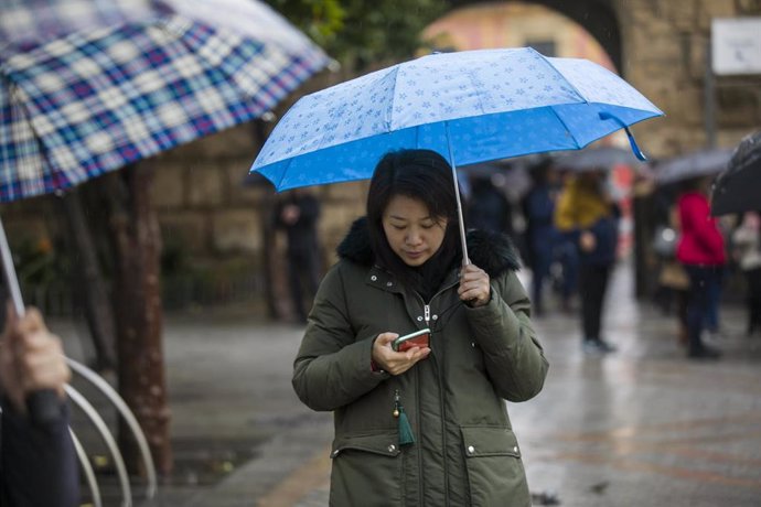 Una mujer mira el móvil mientras sujeta un paraguas