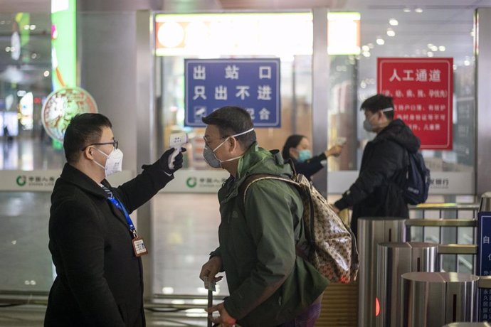 Personal de una estación de tren en China toma la temperatura a un viajero. 