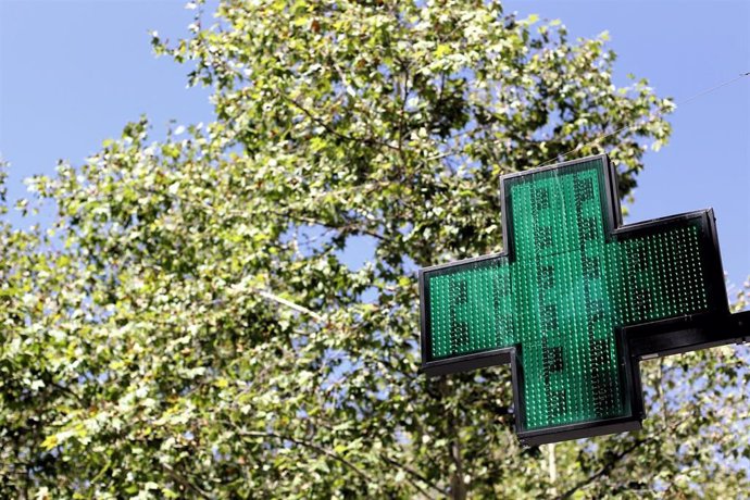Una señal luminosa de la cruz verde a la entrada de una farmacia.