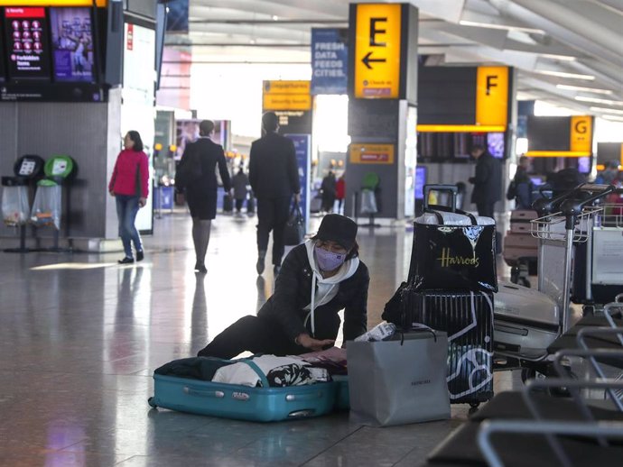 29 January 2020, England, London: A woman wearing a face mask packs her suitcase in the departures area of Terminal 5 at Heathrow Airport, after the British Airways has said that it has suspended all flights to and from mainland China with immediate eff