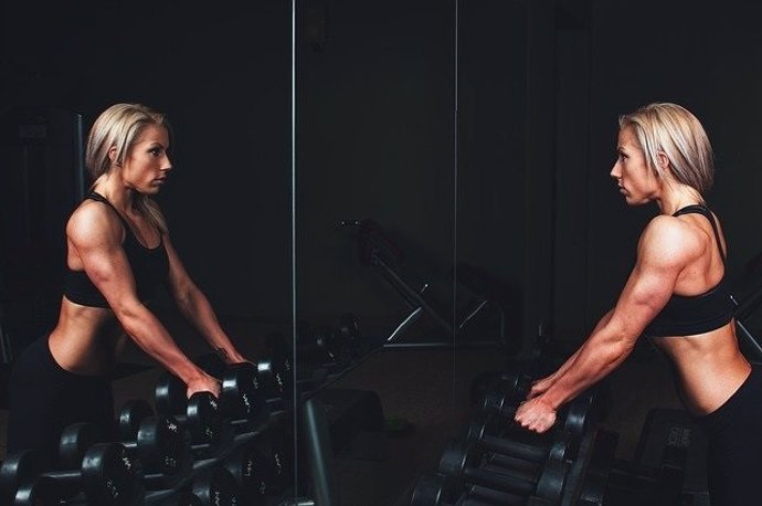 Mujer entrenando musculación se mira al espejo.