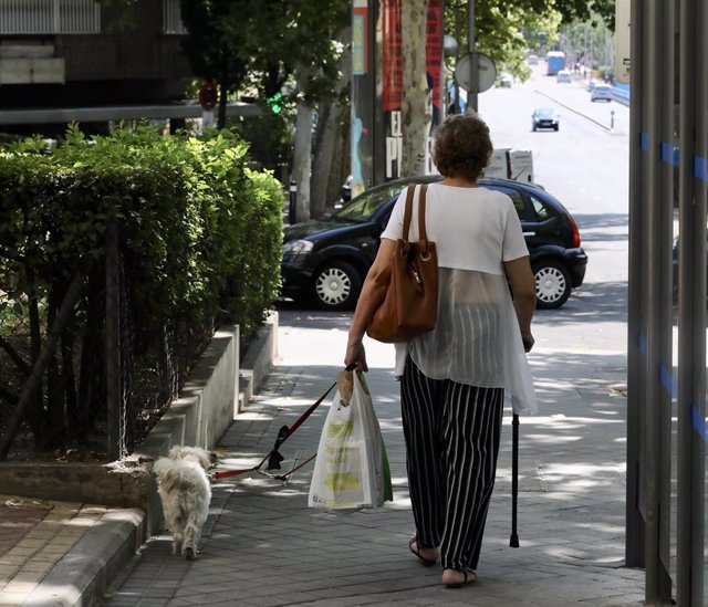 Una mujer de la tercera edad, pasea con su perro por una calle de Madrid.