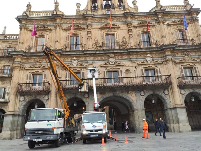 Operarios del servicio de iluminación modifican los focos de la fachada del Ayuntamiento de Salamanca para lucir los colores de la bandera de España este fin de semana.