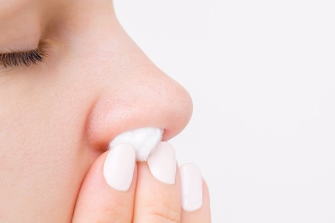 Young woman fingers using cotton wool for stopping blood from nose. Isolated on light gray background. Close up. Side view. Empty place for text.