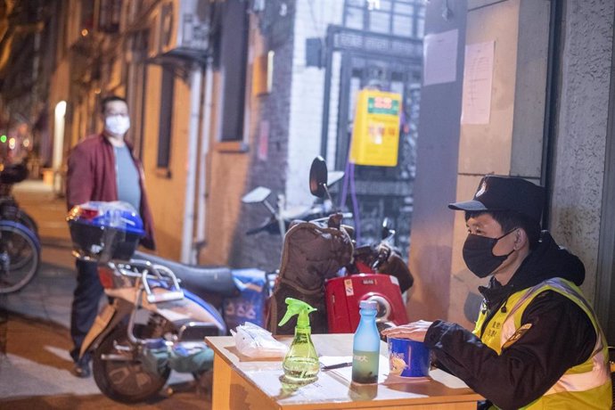 February 10, 2020, Shanghai China - A security guard in a surgical mask sitsbehind a table at the entrance to a residential laneway as he waits to register people and check them for signs of the coronavirus. Although today was China's first day officall