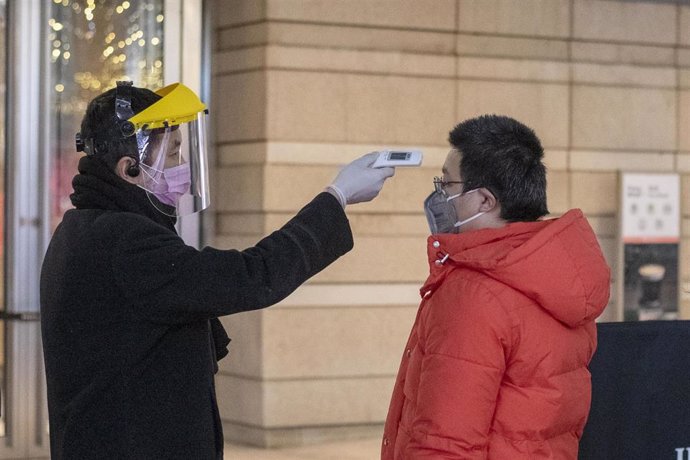 February 10, 2020, Shanghai China - A security guard in a surgical mask and a clear plastic visor uses an electronic thermometer to take the temperature of a man at the entrance to the Kerry Center office block on West Nanjing Road, usually one of Shang