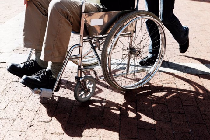 Man in a wheelchair is pushed across parking lot.