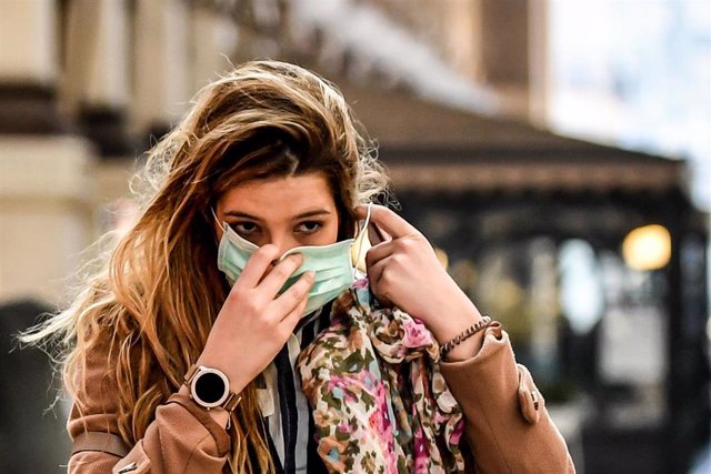 24 February 2020, Italy, Milan: A pedestrian puts on a surgical mask on her face amid the outbreak of the coronavirus. Photo: Claudio Furlan/LaPresse via ZUMA Press/dpa