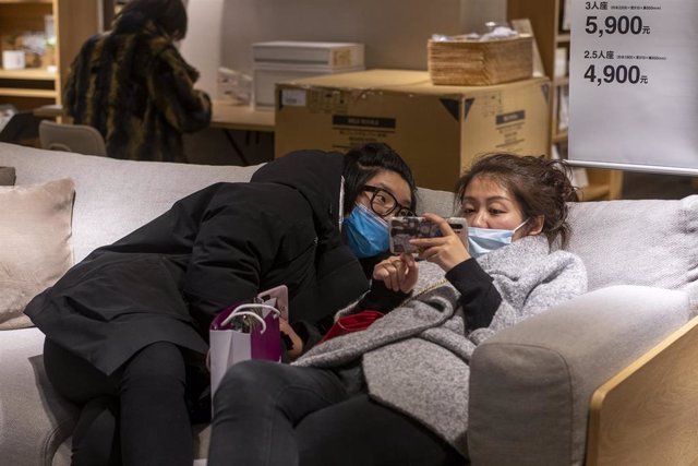 Dos mujeres ataviadas con mascarillas prueban la comodidad de un sofá en una tienda de muebles de Shanghai.