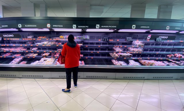 Una mujer observa los alimentos que quedan en los refrigeradores de carne de un supermercado un día marcado por colas de gente deseosas de hacer acopio de alimentos.