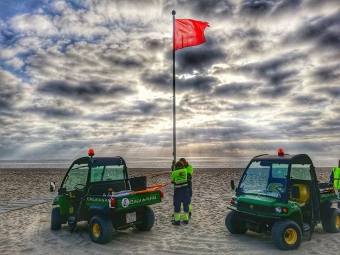 Operarios municipales izan una bandera roja en una playa del municipio.