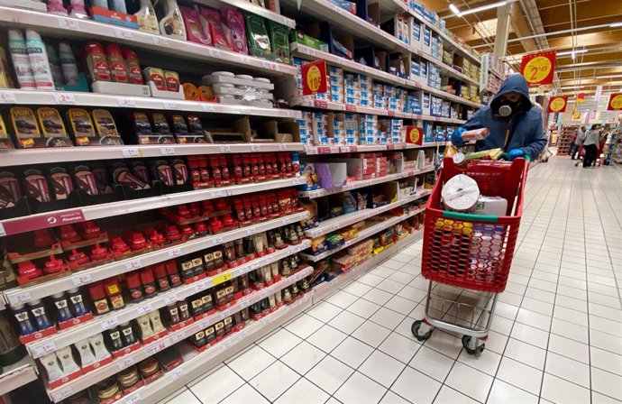 Un hombre cubierto con una mascarilla coge productos de las estanterías de un supermercado de Madrid