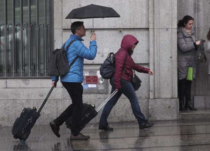 Dos turistas se refugian de la lluvia con paraguas, en Madrid (España)