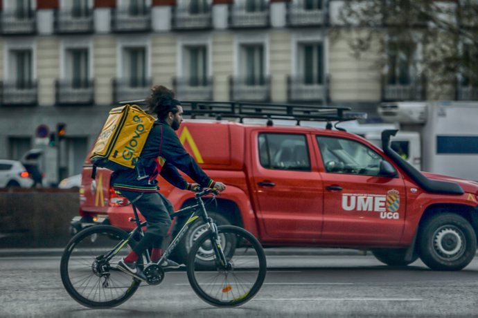 Un repartidor en bici circula por una calle de Madrid al lado de un vehículo de la UME el 25 de marzo de 2020.