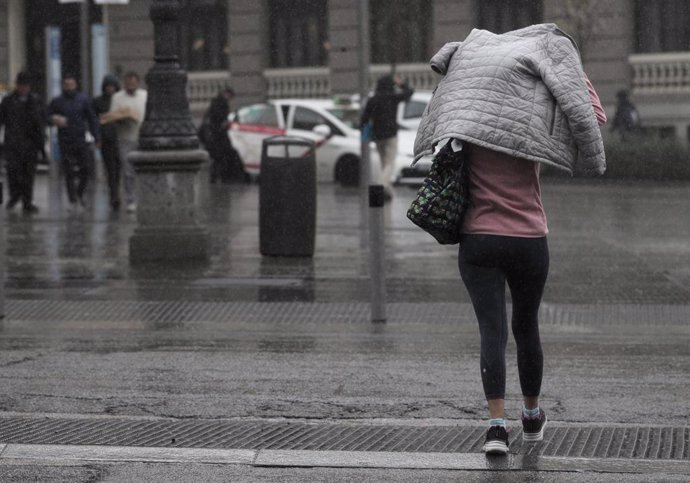 Una mujer se tapa con el abrigo para refugiarse de la lluvia, en Madrid (España), a 5 de marzo de 2020.