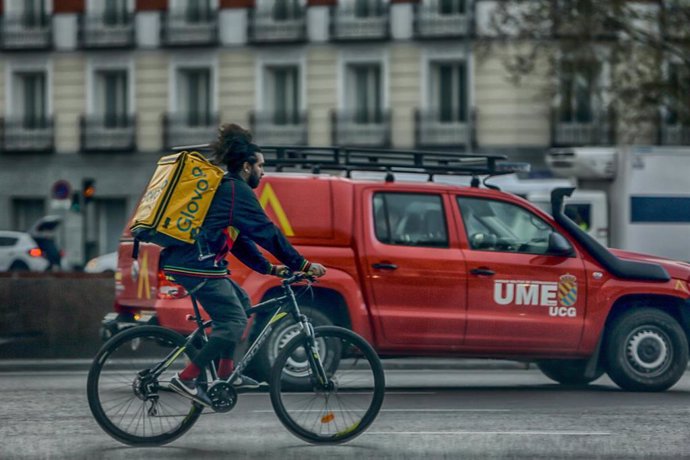 Un repartidor en bici circula por una calle de Madrid al lado de un vehículo de la UME el 15 de marzo de 2020.