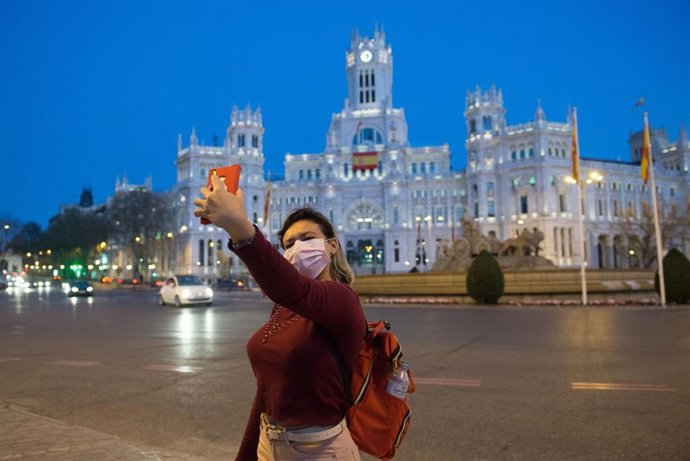 Una joven protegida con mascarilla se realiza una fotografía en La Cibeles en plena crisis del coronavirus 