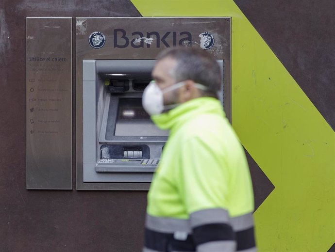 Un trabajador (con chaleco y mascarila) pasa delante de un cajero de Bankia