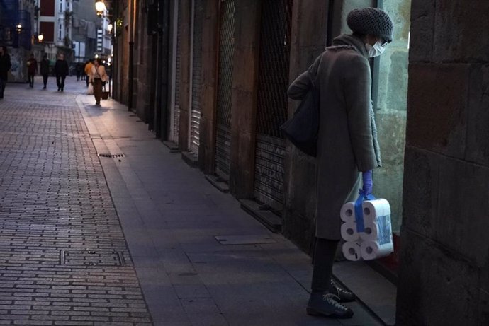 Una mujer protegida con mascarilla y con un paquete de papel higiénico en la mano pasea por Bilbao tras la declaración de Estado de Alarma en todo el país por el avance del coronavirus, en Bilbao, Vizcaya, País Vasco (España).