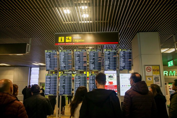 Varias personas comprueban la llegada de vuelos en varios paneles luminosos en aeropuerto Adolfo Suárez Madrid-Barajas. 