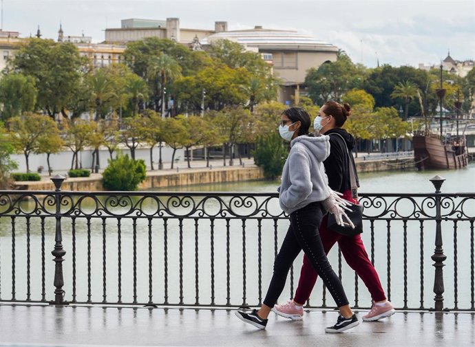 Dos jovenes con mascarillas paseando andando por el puente de Triana en el tercer día de alarma. Sevilla a 17 de marzo 2020