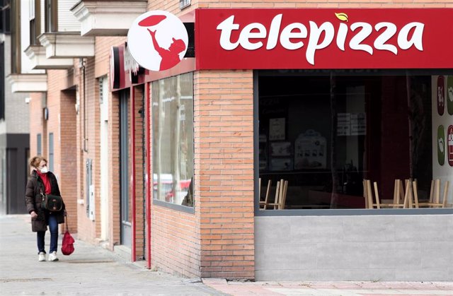 Una mujer protegida con mascarilla pasea cerca de un local de Telepizza el mismo día en el que han comenzado a servir menús para alumnos madrileños con beca comedor y así evitar que les falten alimentos por la crisis del coronavirus, en Madrid.